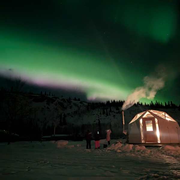 Northern lights over snowy landscape with tent and smoke.