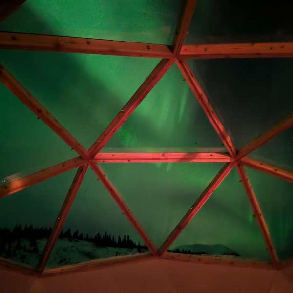 Northern lights seen through a geodesic dome's glass panels at night.